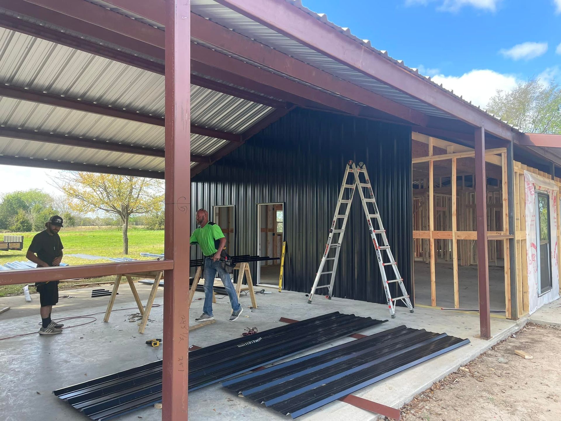Workers building a metal shed frame with ladders and roofing panels in a yard