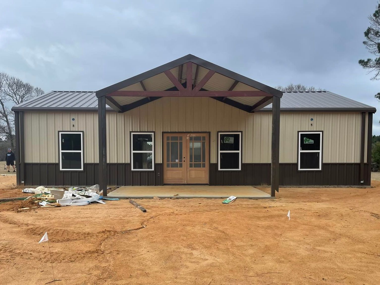 New tan-and-brown metal building with a central entrance on a dirt lot under cloudy skies