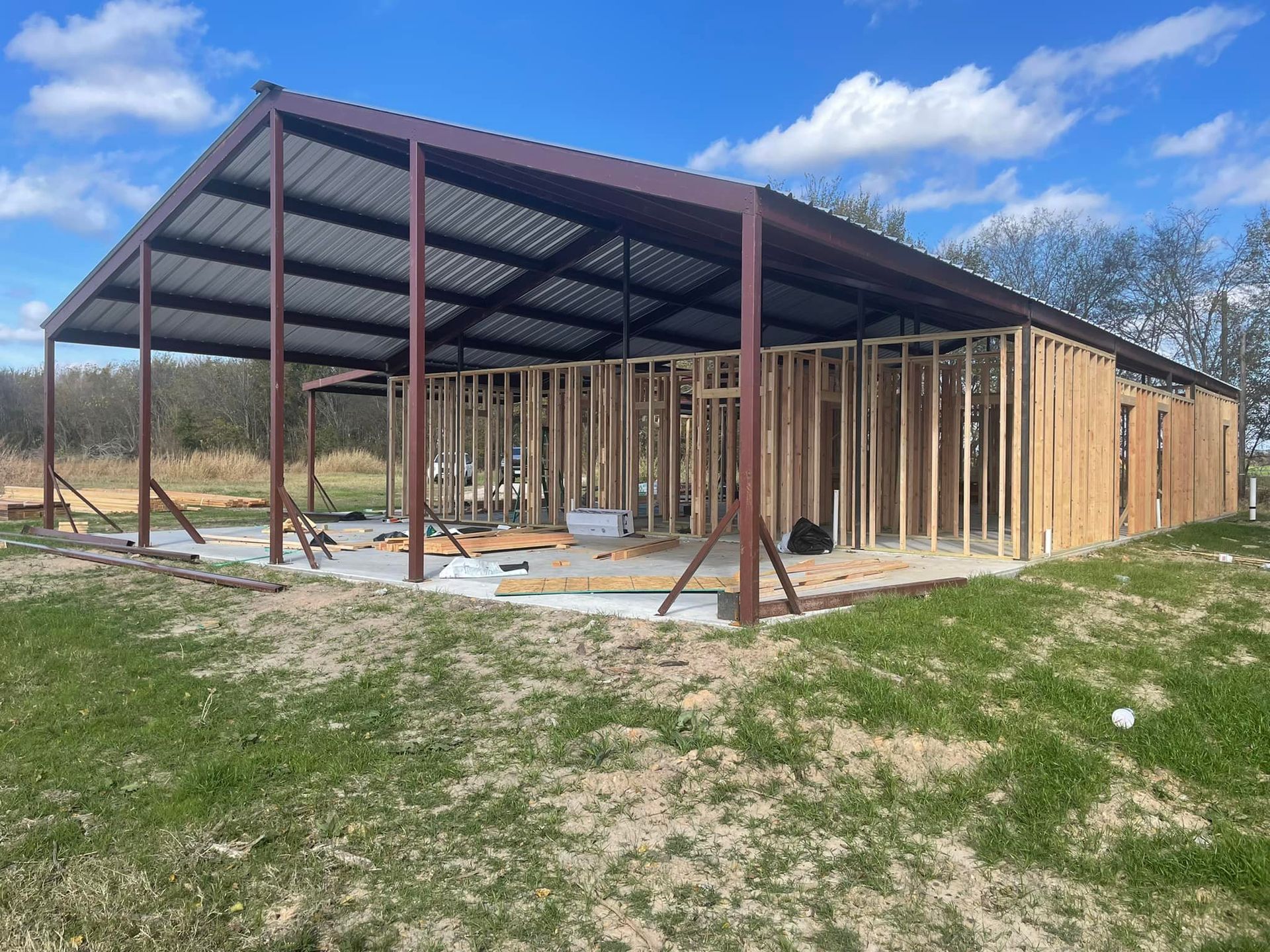 Partially built metal-framed structure with wooden walls in an open grassy field under a blue sky