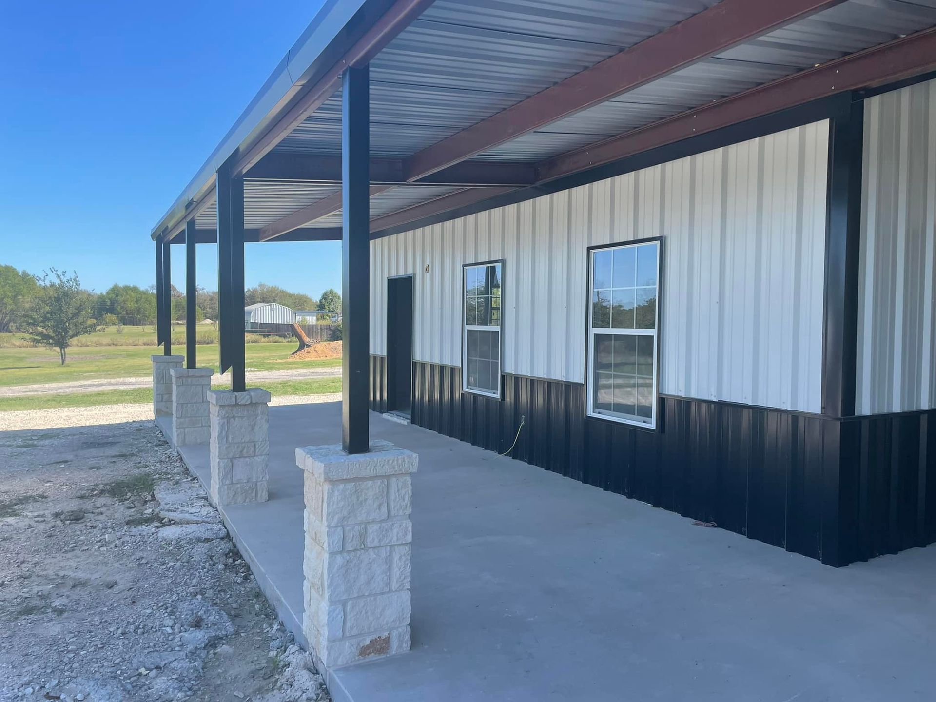 Exterior of a white-and-black metal building with a covered porch and concrete posts