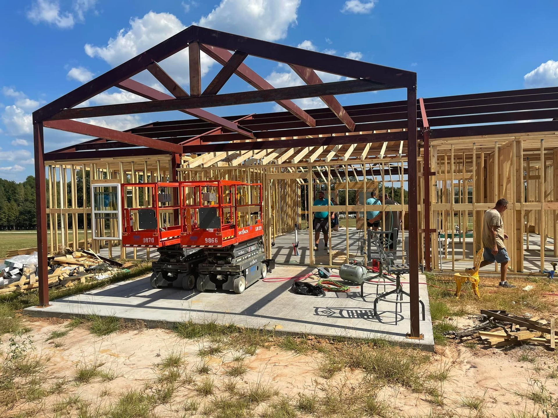 Construction site with wooden house framing and a red utility cart under a steel canopy