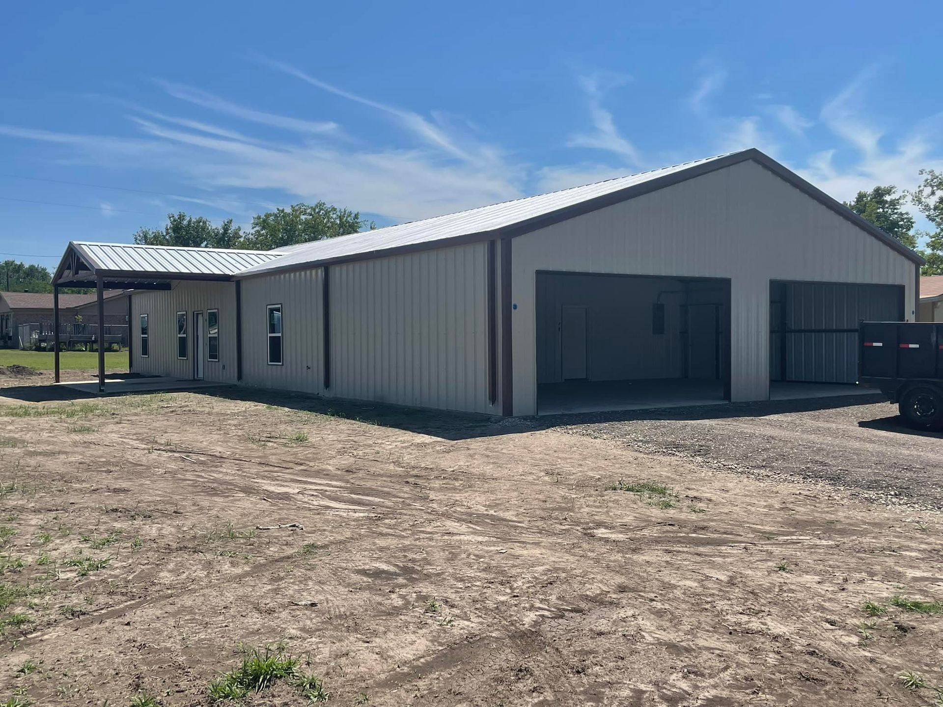 Large white metal building with a gabled roof on a dirt lot under a blue sky