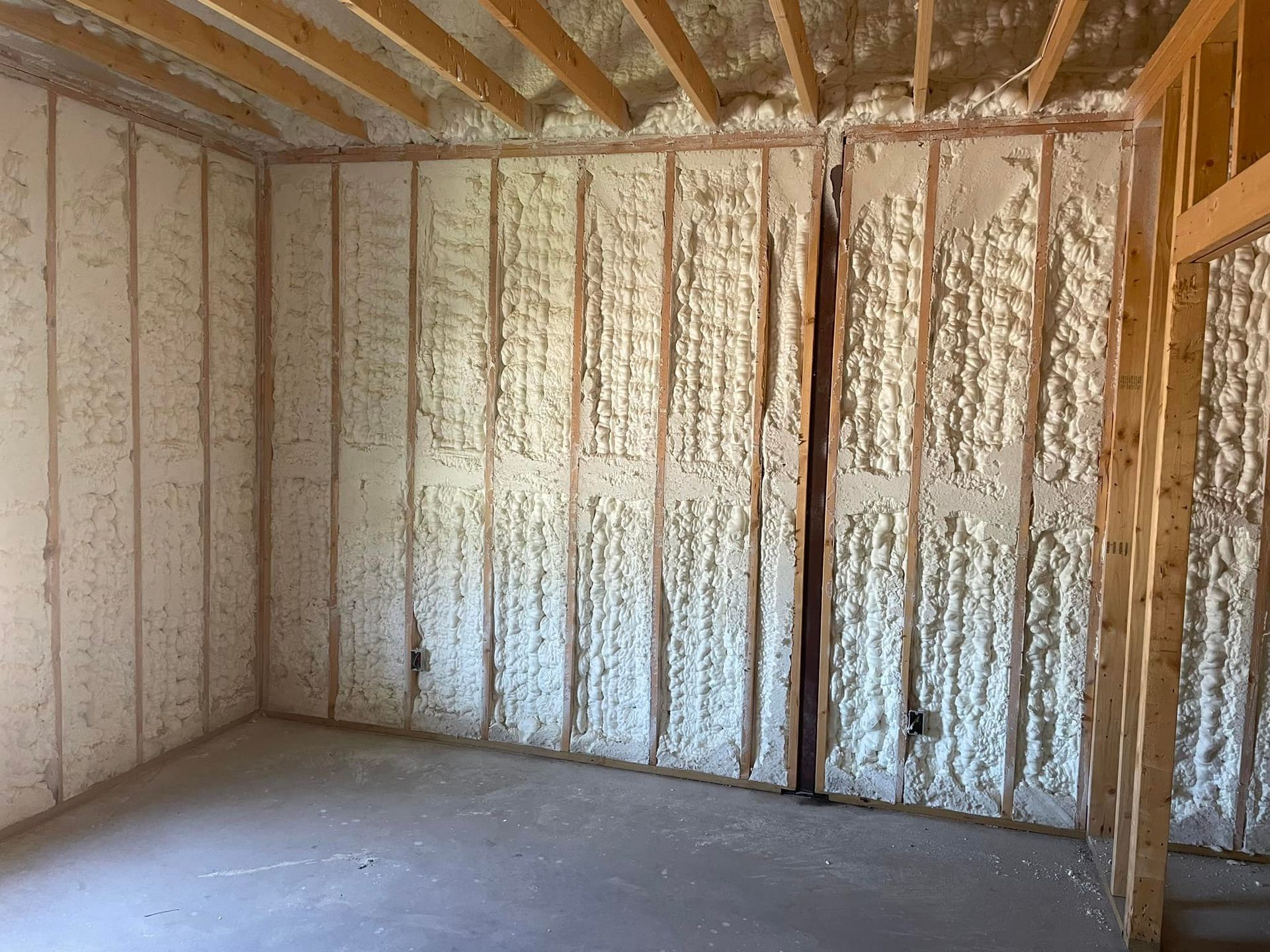 Insulated unfinished room with exposed wood framing and spray foam on walls and ceiling