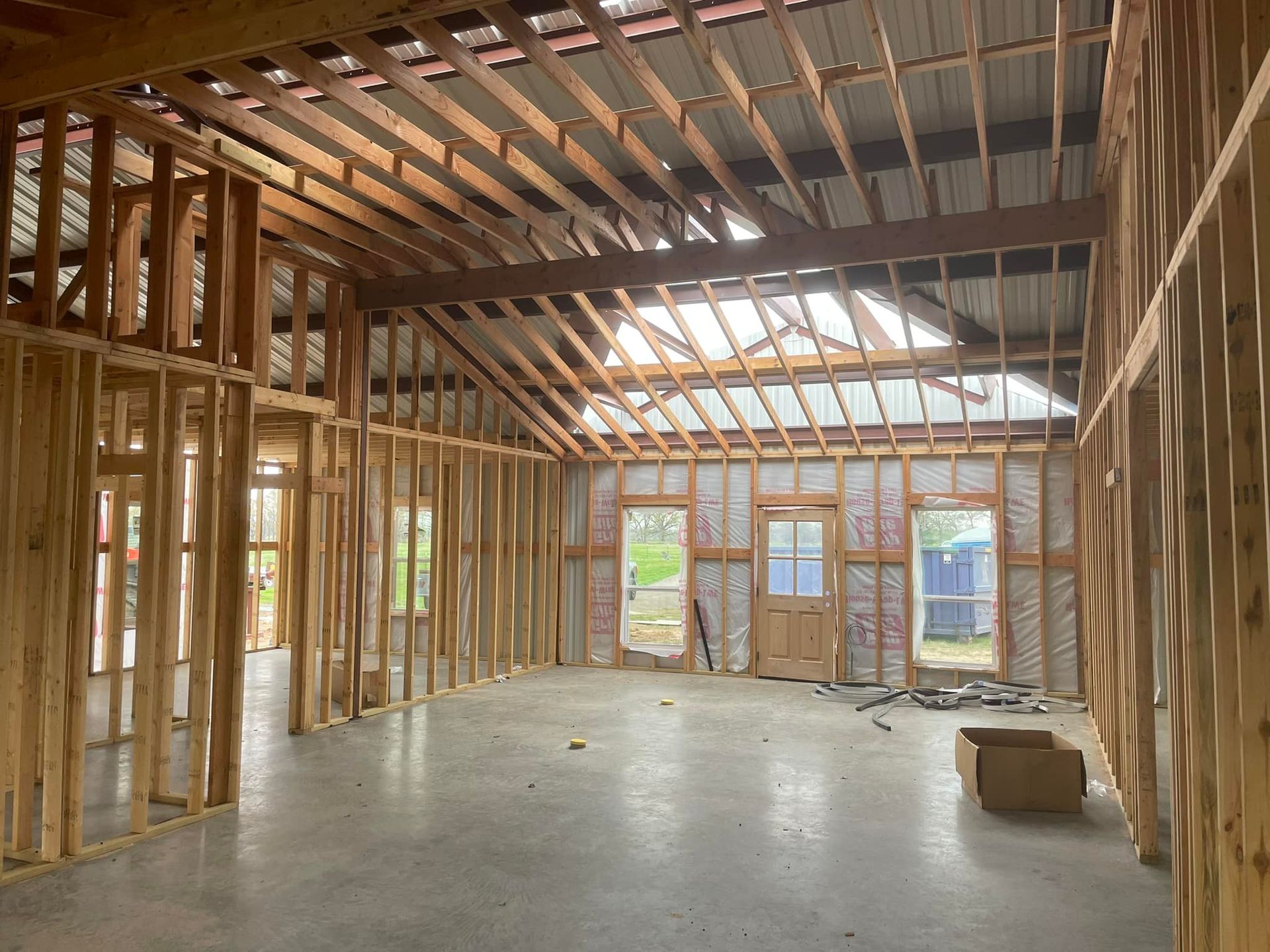 Unfinished wooden house interior with exposed framing, vaulted ceiling, and concrete floor.