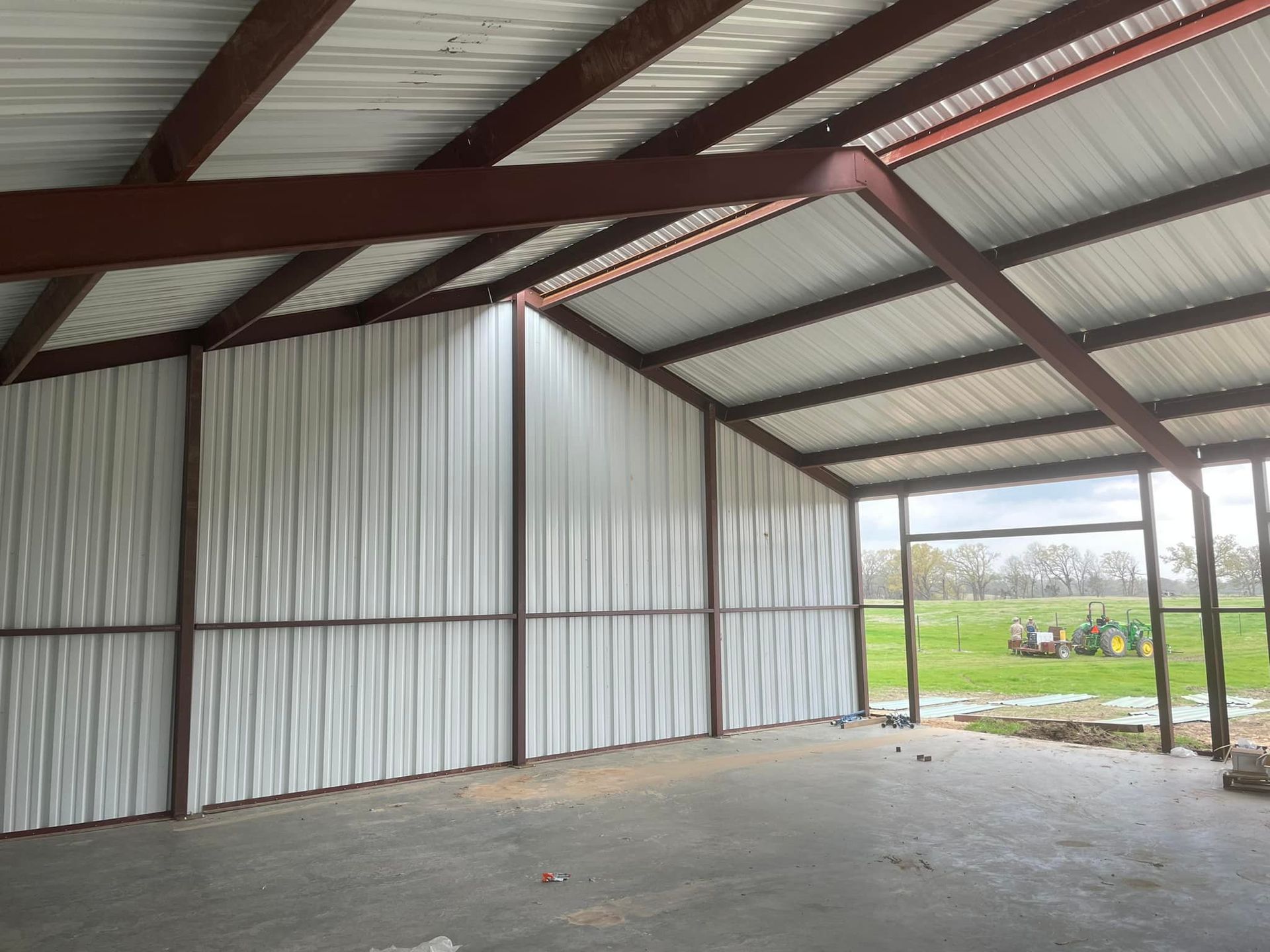 Empty metal barn interior with corrugated walls, open side, and concrete floor