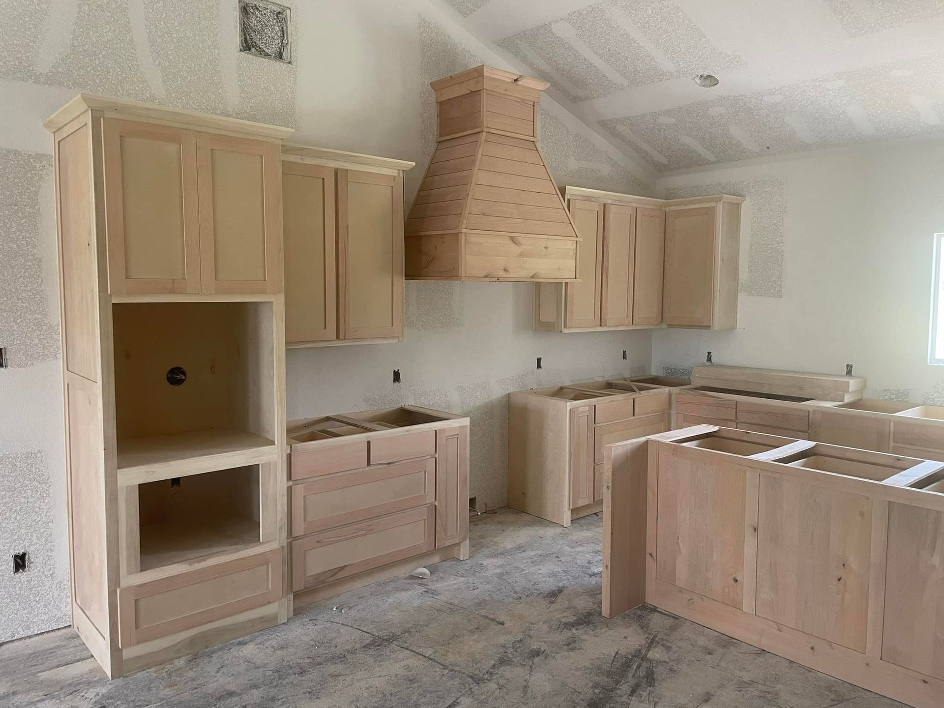 Unfinished kitchen with light wood cabinets, a range hood, and a partially installed island on a tiled floor