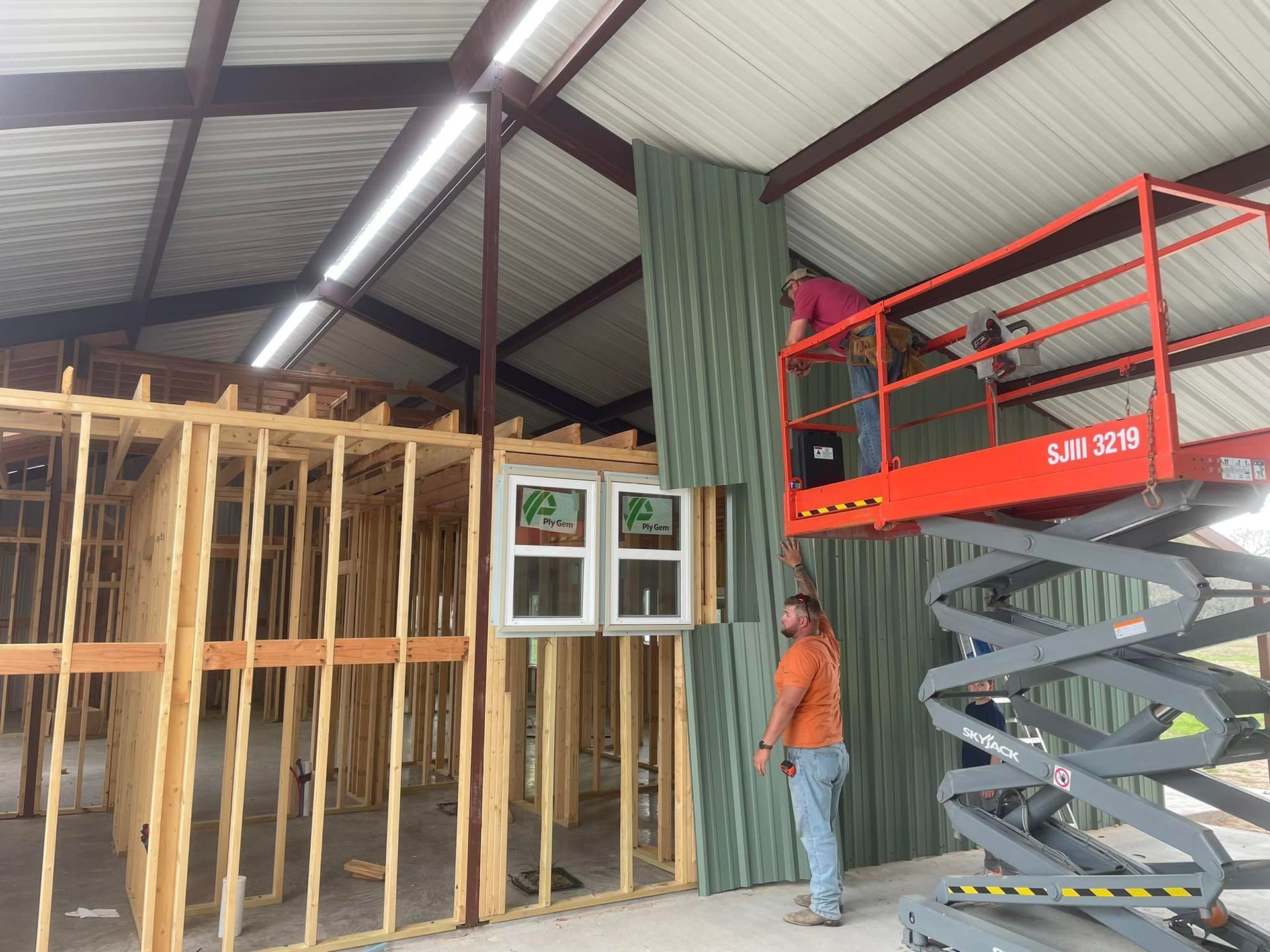 Construction site interior with exposed framing and a worker beside a red scissor lift