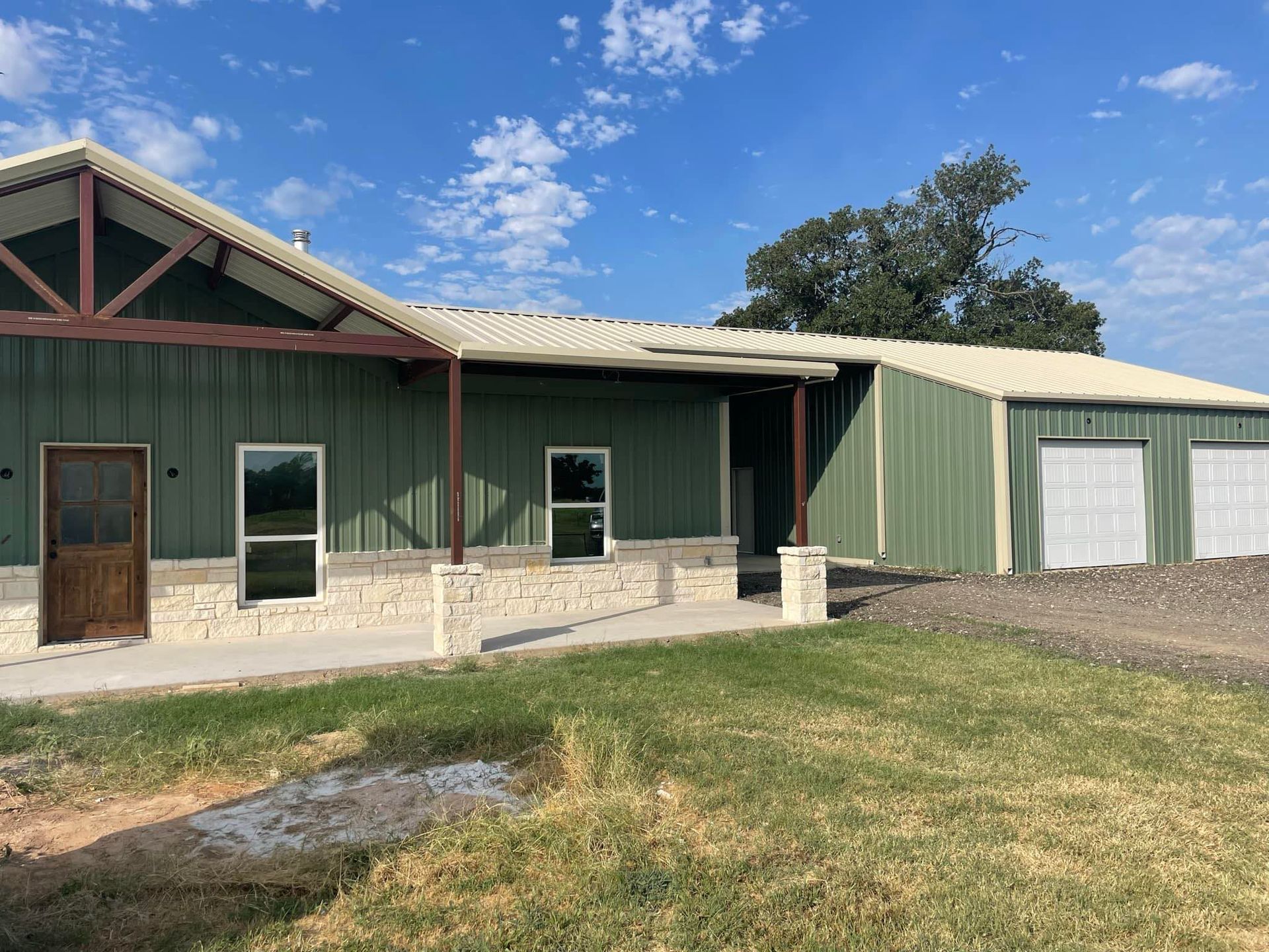 Green metal building with stone base and garage doors under a blue sky.