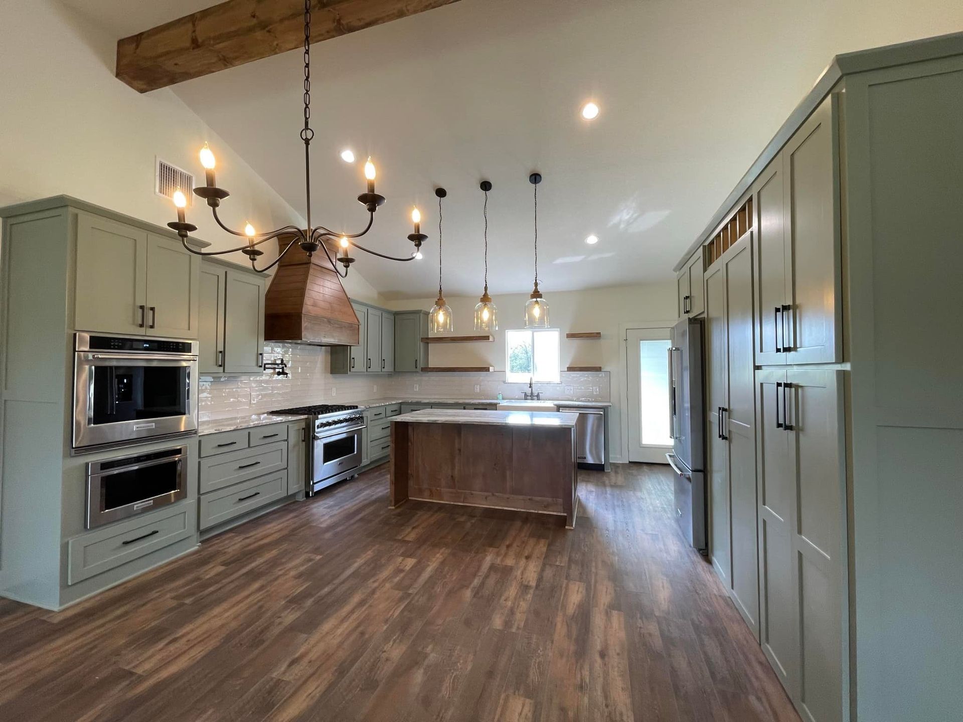 Spacious modern kitchen with sage cabinets, wood island, pendant lights, and stainless steel appliances.