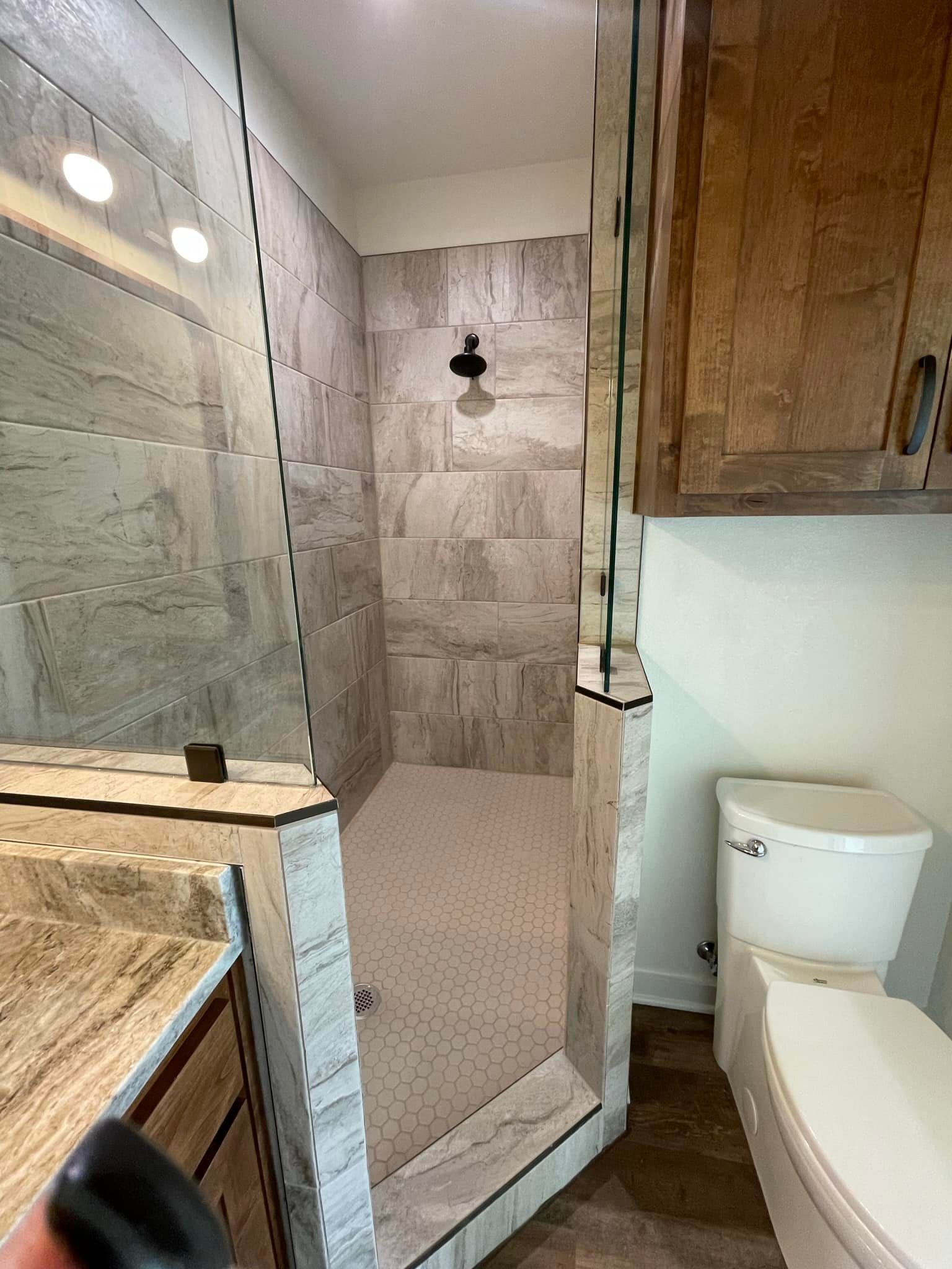 Bathroom with glass shower, tiled walls, and a toilet beside a wooden cabinet.
