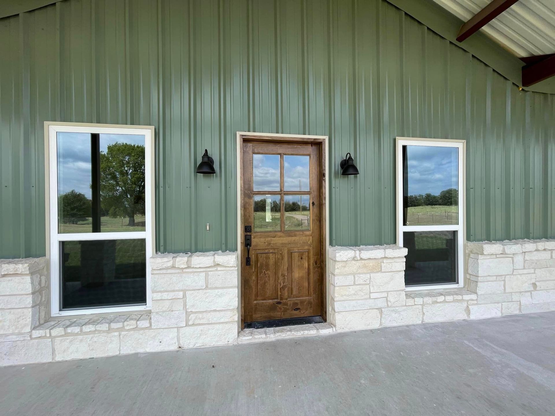Front view of a green building with white stone base, wooden door, and two windows