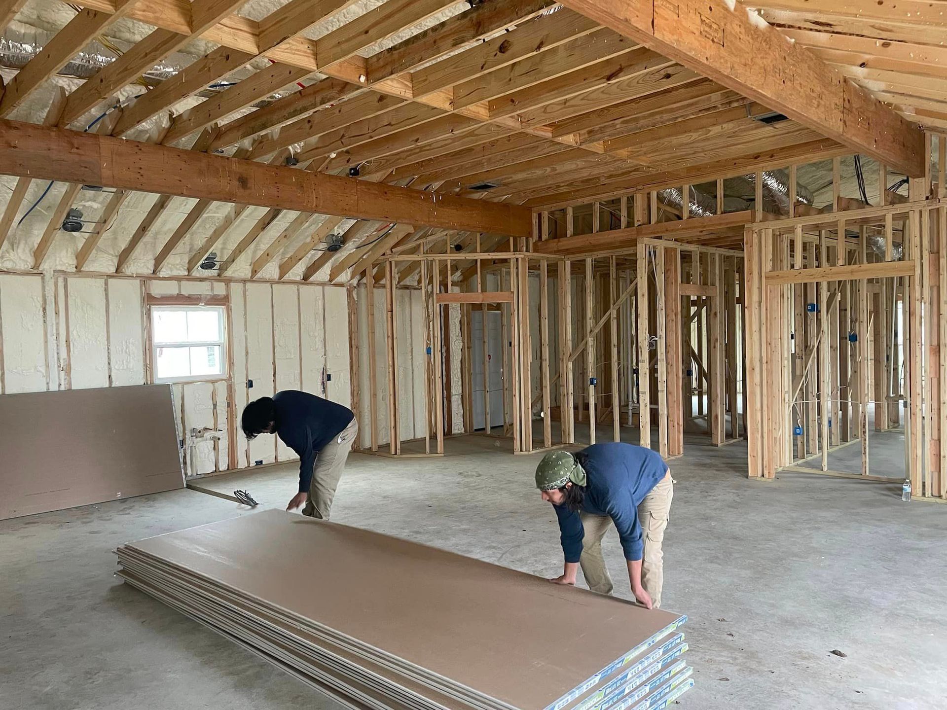 Two workers installing drywall in a framed house under construction