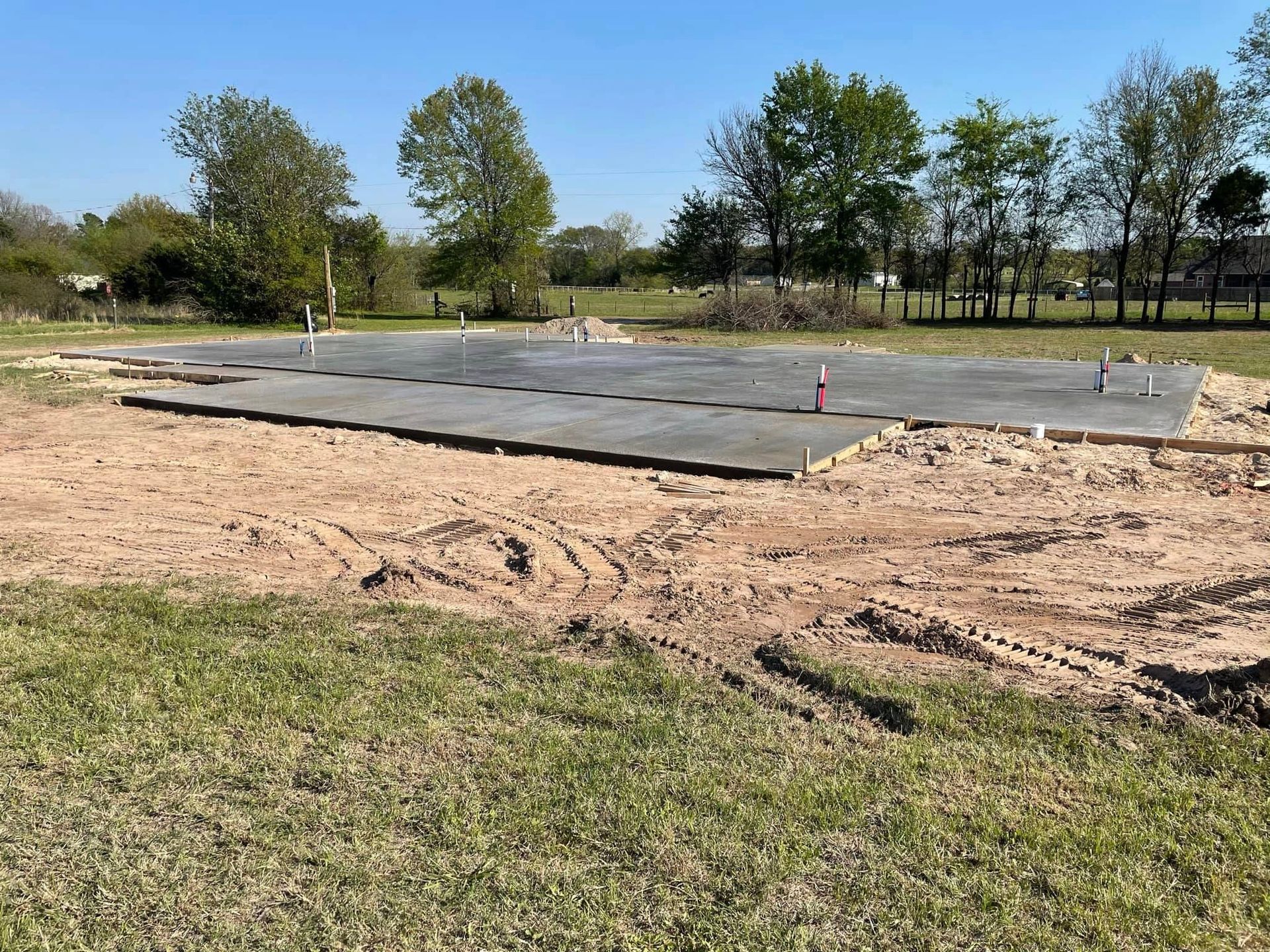 Concrete slab foundation site with dirt foreground and trees in the background
