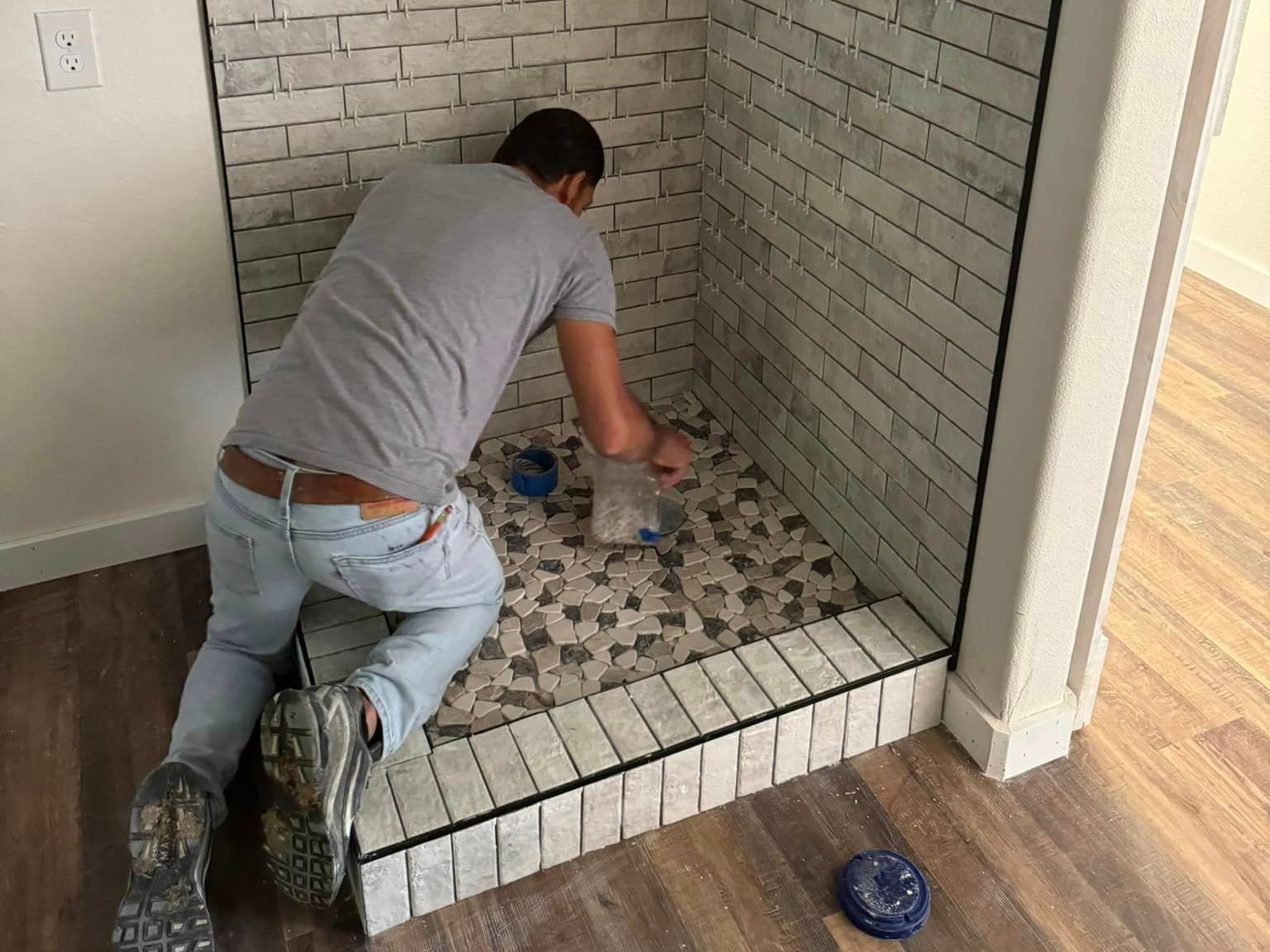 Person kneeling and tiling a small shower floor and bench with mosaic tiles