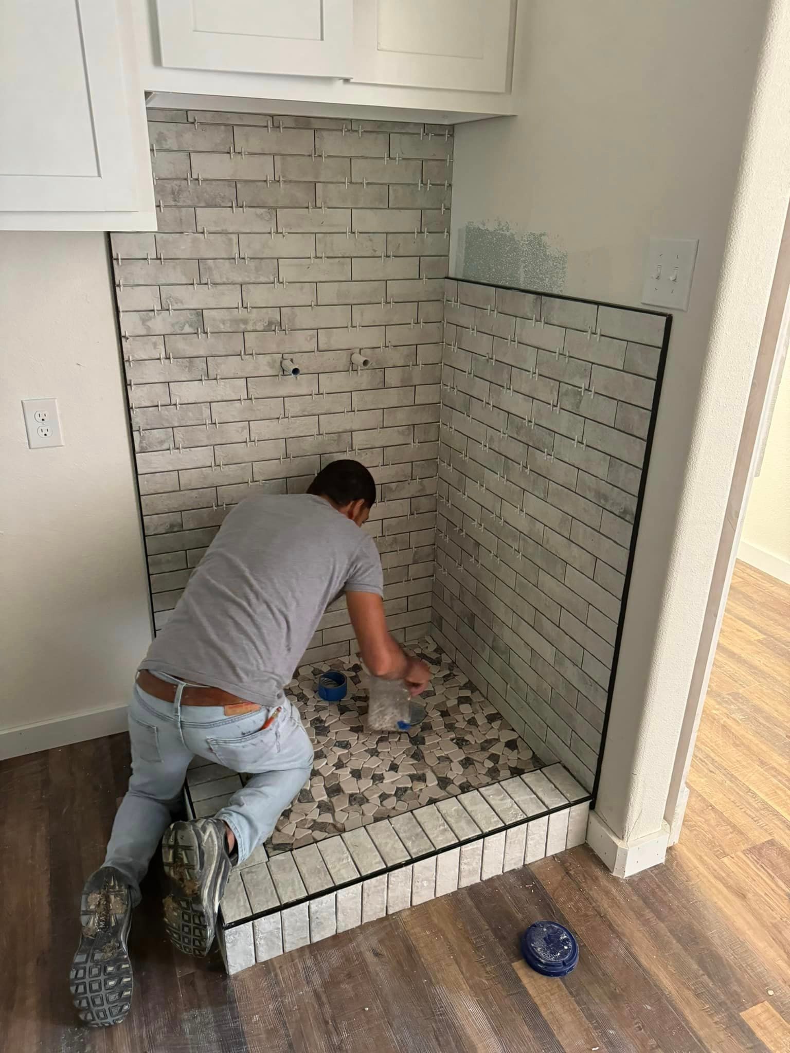 Worker installing white subway tile in a small shower alcove