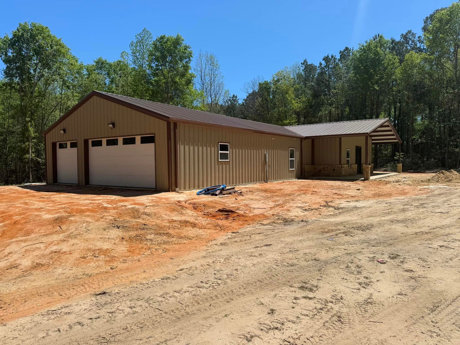 Tan metal-sided house with attached garage on a dirt lot under a clear blue sky