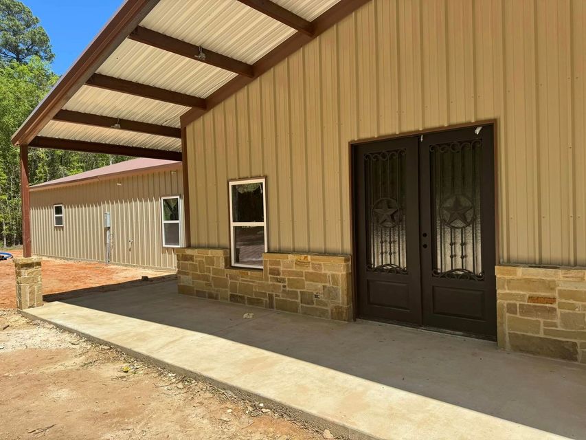 Tan metal-sided building with stone base, covered porch, and double doors on a concrete walkway