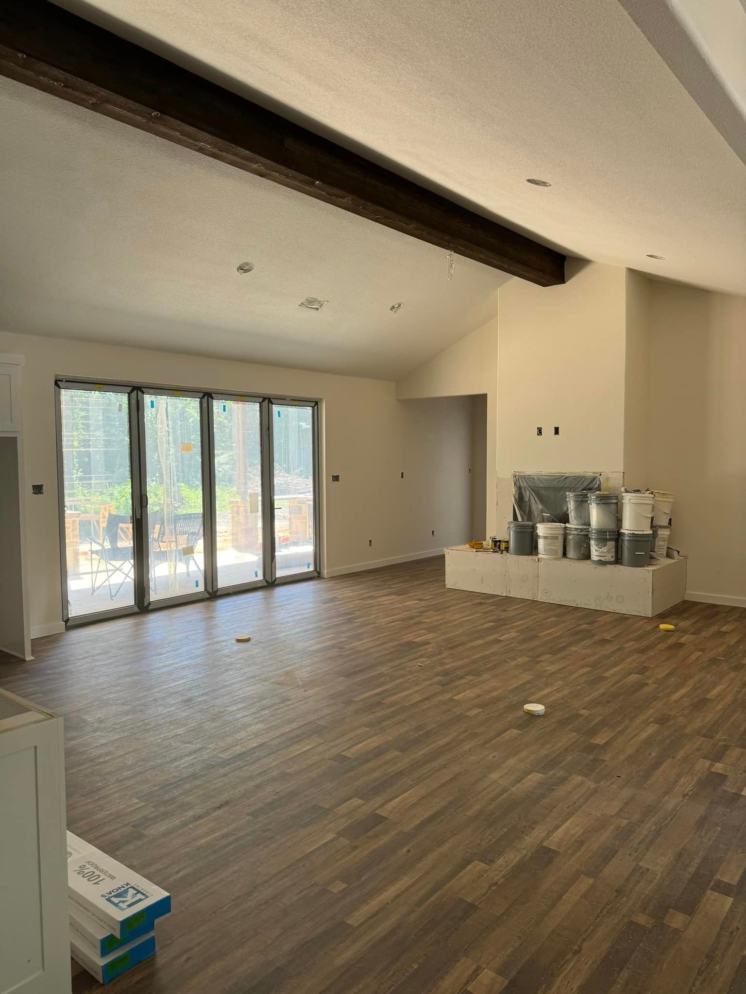 Empty modern living room with wood floors, exposed beam ceiling, and large glass doors opening to a patio.