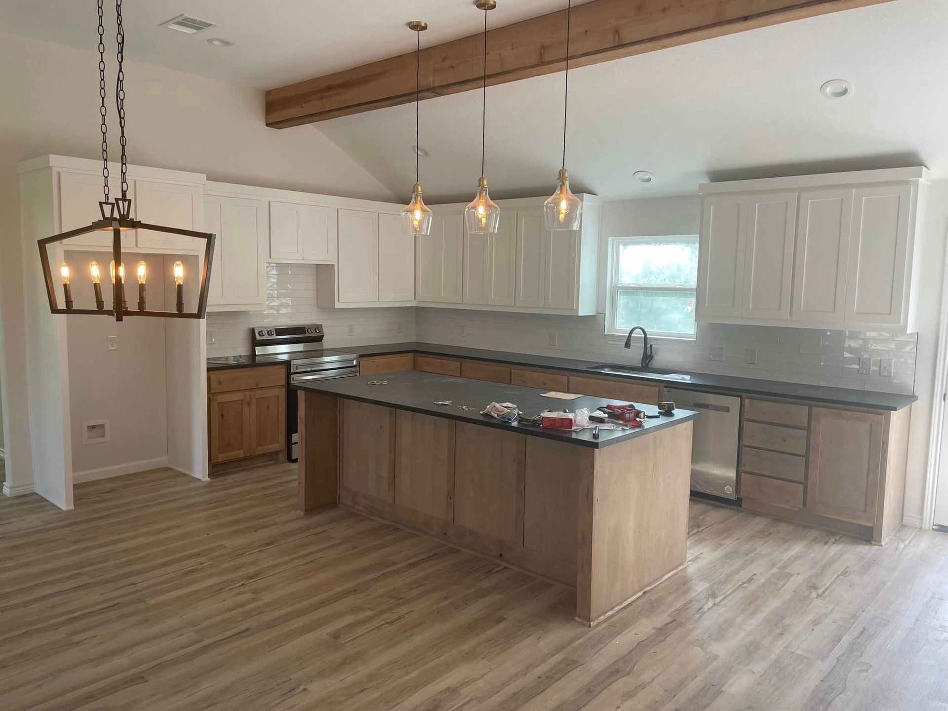Bright kitchen with white cabinets, gray island, wood floor, and pendant lights.