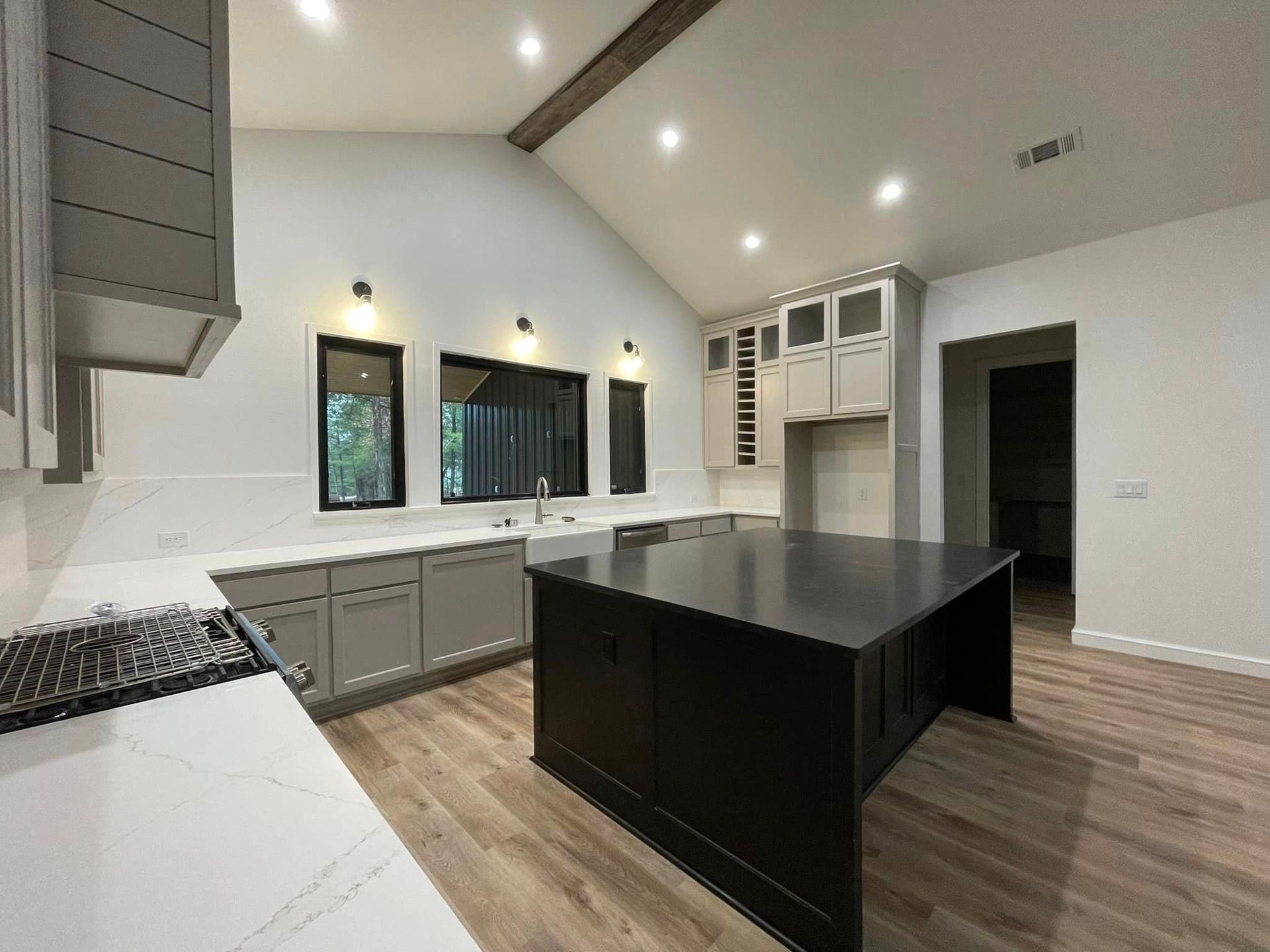 Modern kitchen with white cabinets, black island, wood floors, and vaulted ceiling with recessed lights