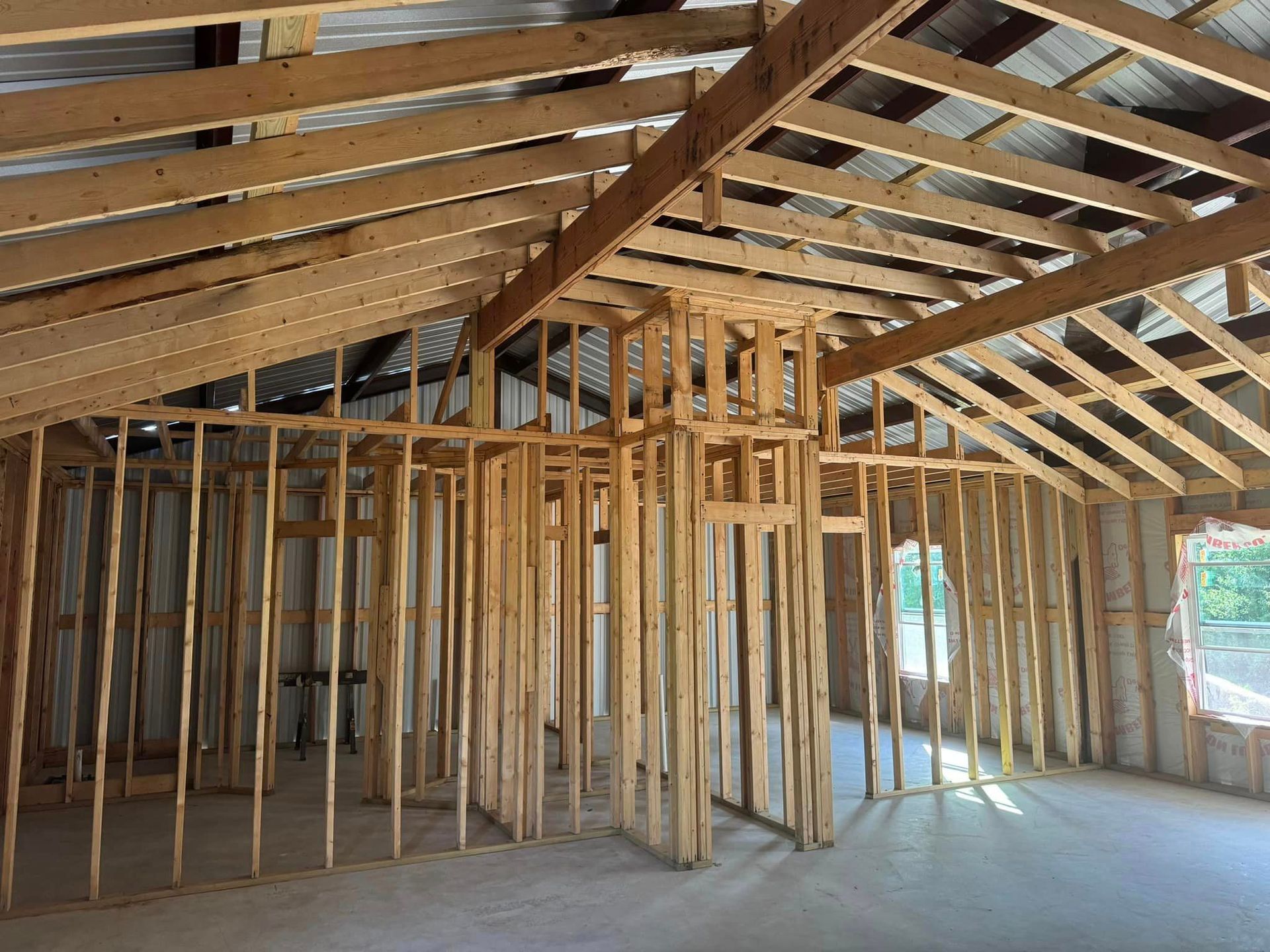 Framed house interior with exposed wood studs and rafters, unfinished walls, and concrete floor