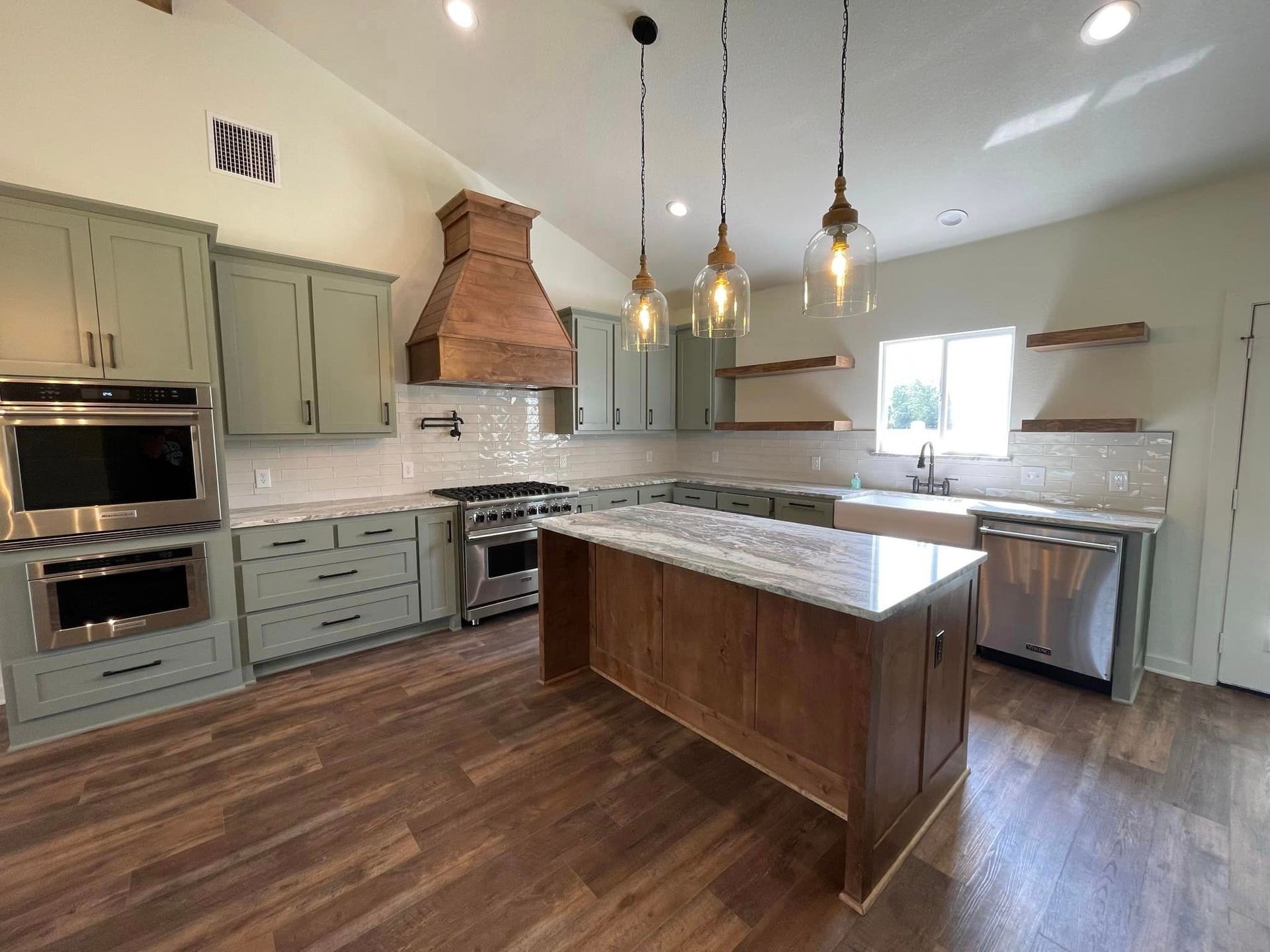 Modern kitchen with gray cabinets, wood floors, marble island, pendant lights, and copper range hood