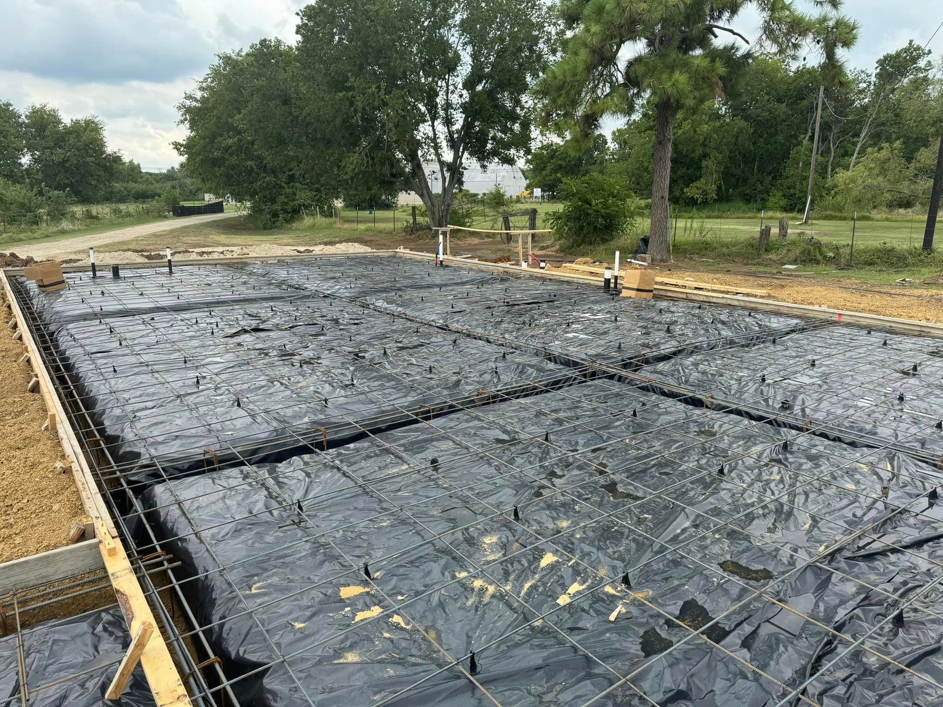 Concrete foundation slab covered with black plastic sheeting at a rural construction site