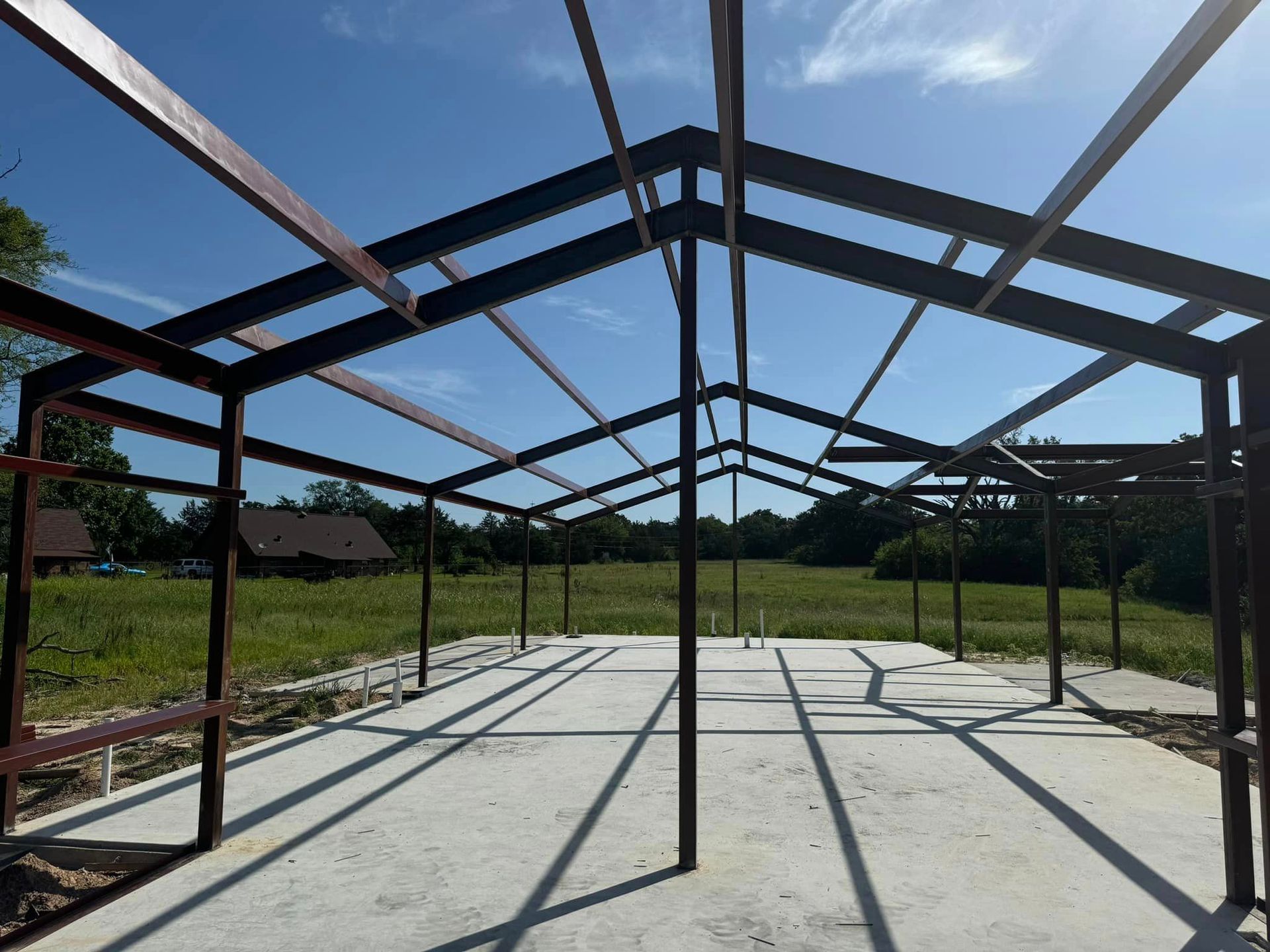 Steel frame of an unfinished building on a concrete slab under a blue sky