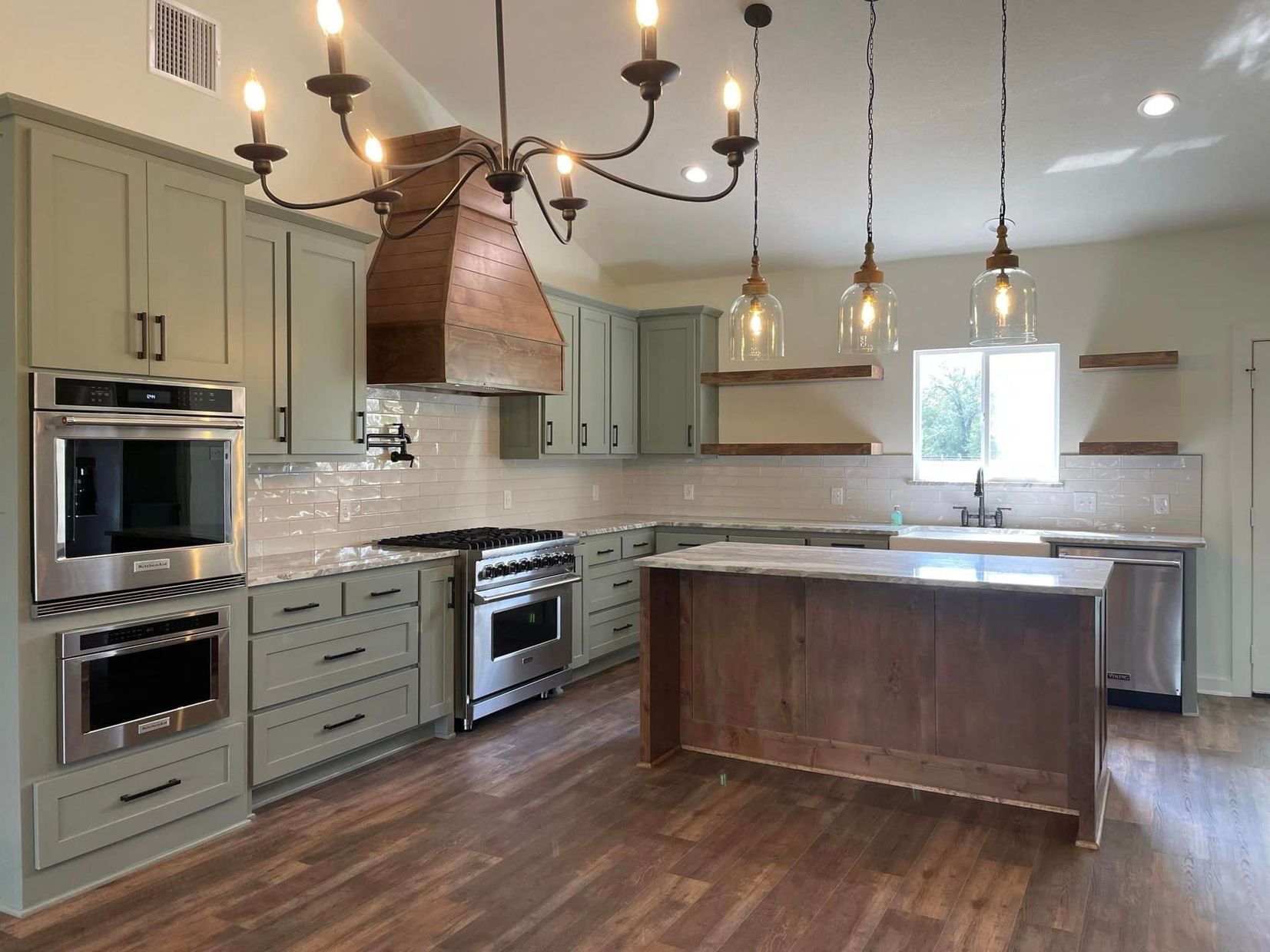 Modern kitchen with sage cabinets, dark wood island, stainless appliances, and pendant lights