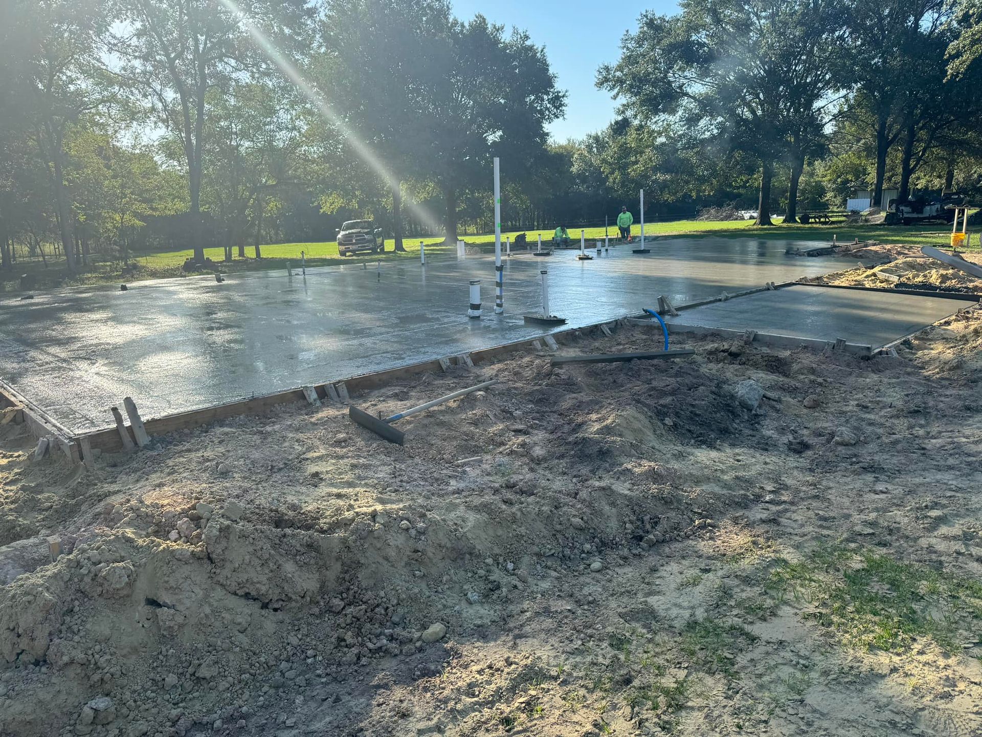 Concrete slab under construction in a sunny park, with wet cement and trees in the background
