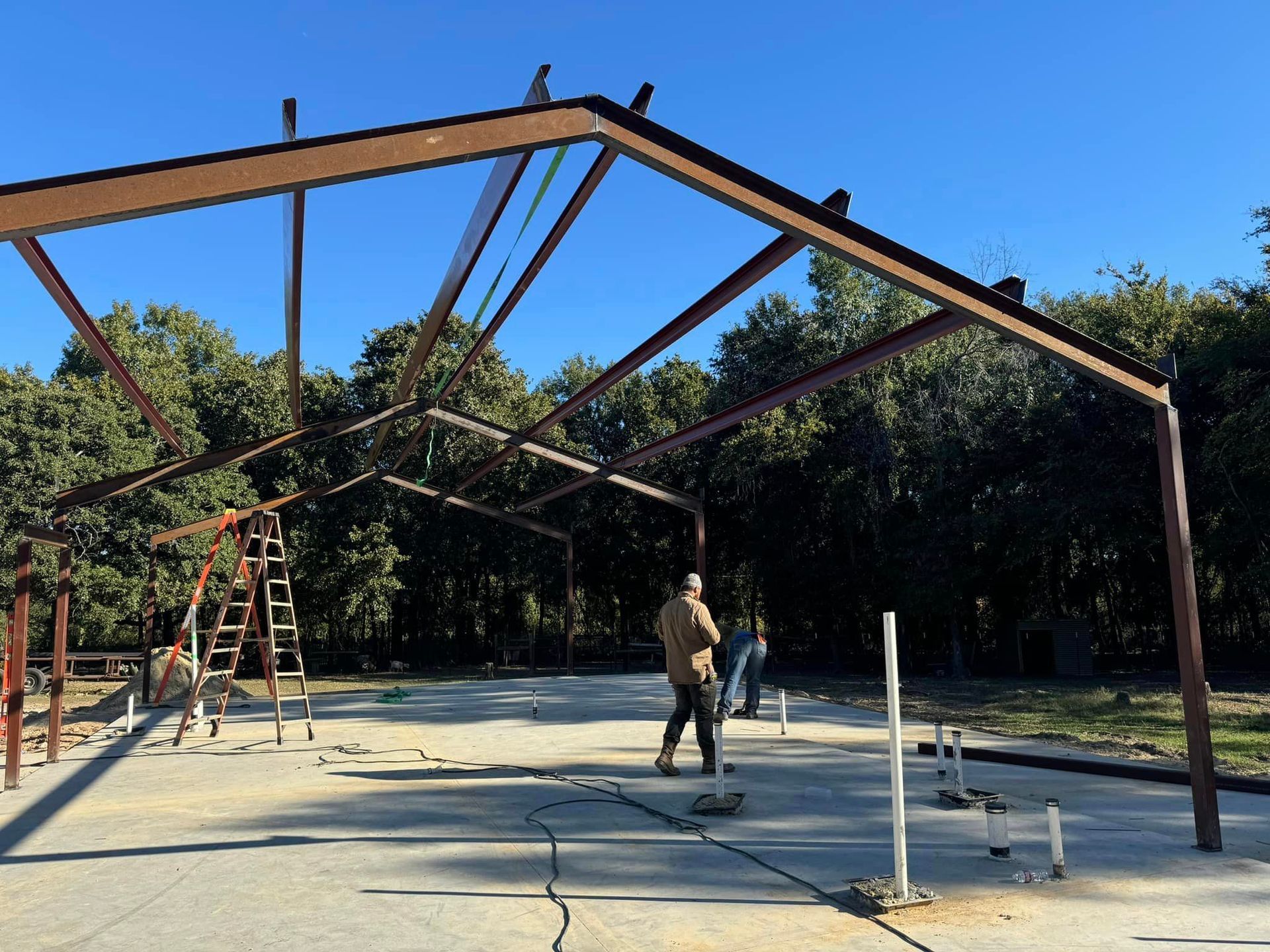 Steel frame structure under construction with workers and a ladder outdoors under a blue sky
