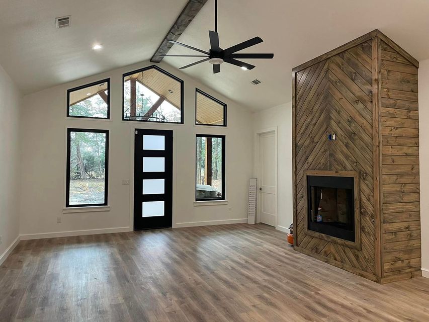 Empty living room with vaulted ceiling, black ceiling fan, modern front door, and brick fireplace accent wall