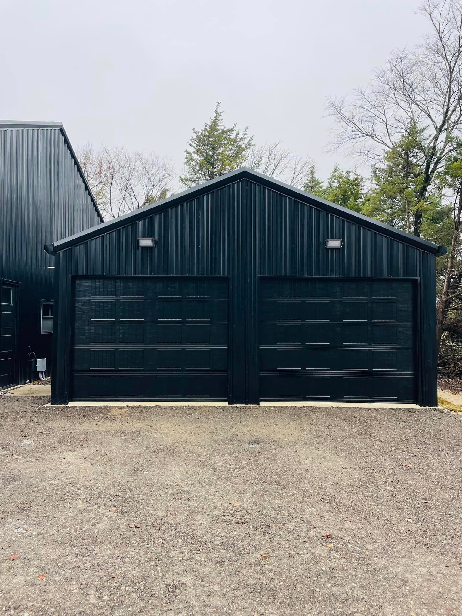 Dark green double garage with gravel driveway and trees in the background