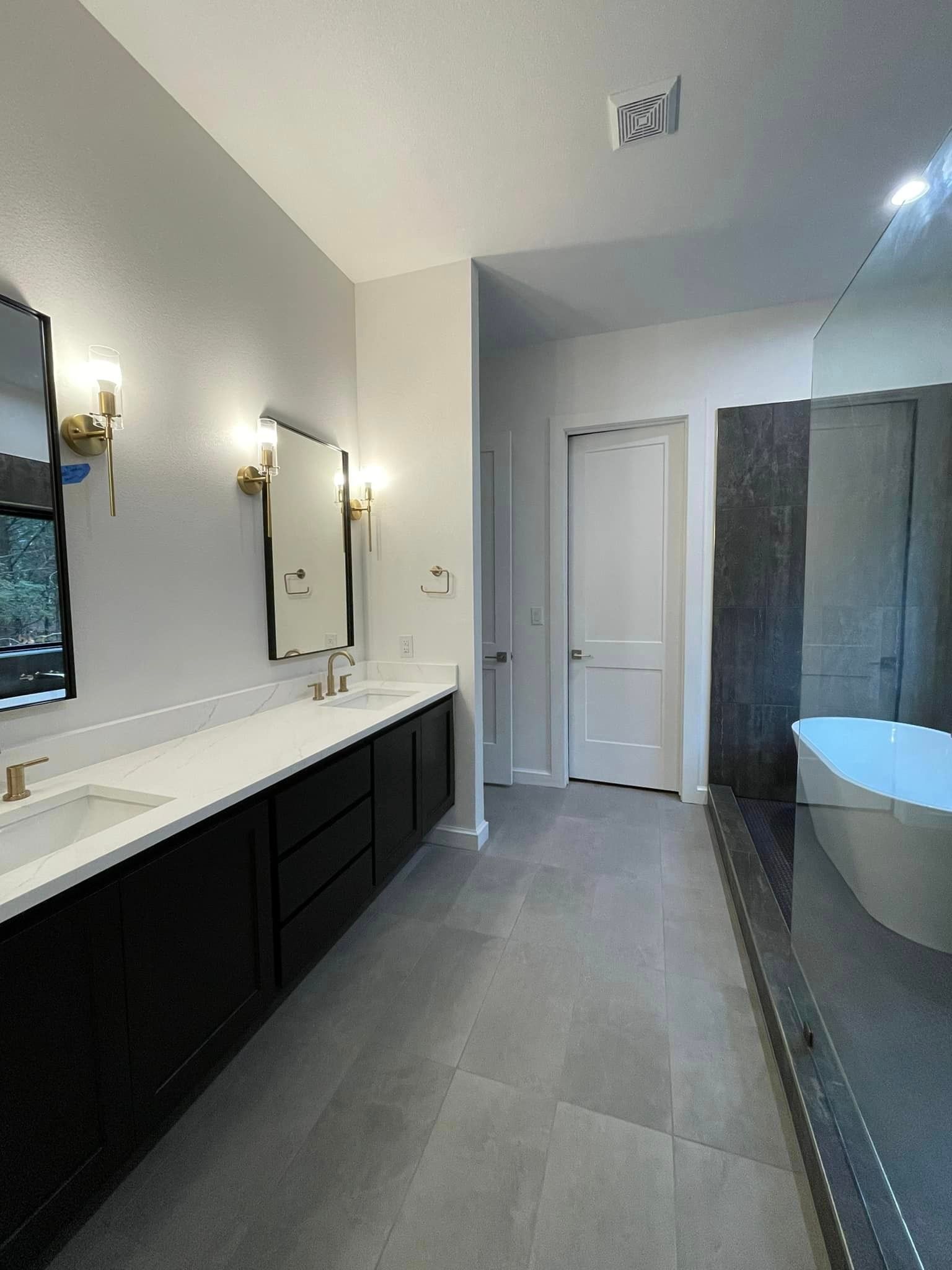 Modern bathroom with double vanity, wall sconces, walk-in shower, and a freestanding tub