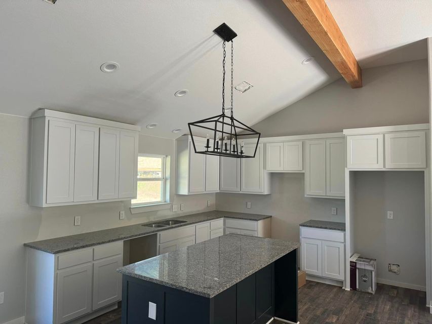 Bright kitchen with white cabinets, granite island, stainless appliances, and hanging light fixture.