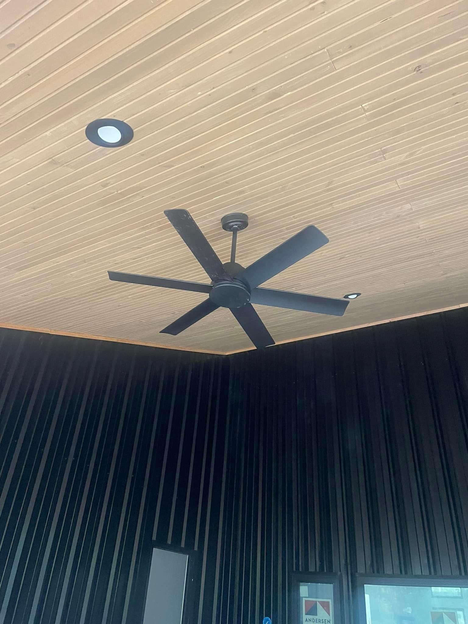 Indoor ceiling with a dark ceiling fan, recessed light, and dark ribbed walls below.