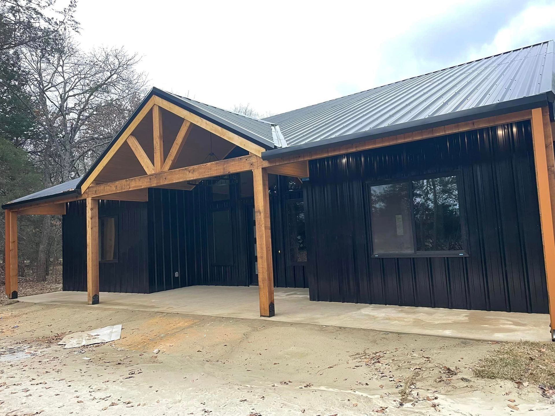 Rustic black wooden building with a metal roof and timber porch in a bare dirt lot