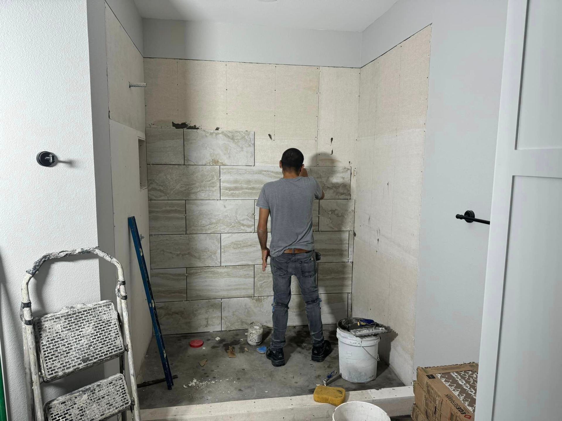 Worker painting a beige wall in a small room under renovation