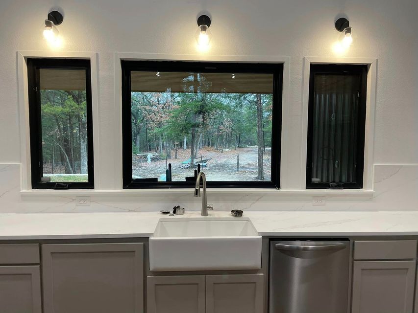 Modern kitchen with white sink centered under three windows and gray cabinets below