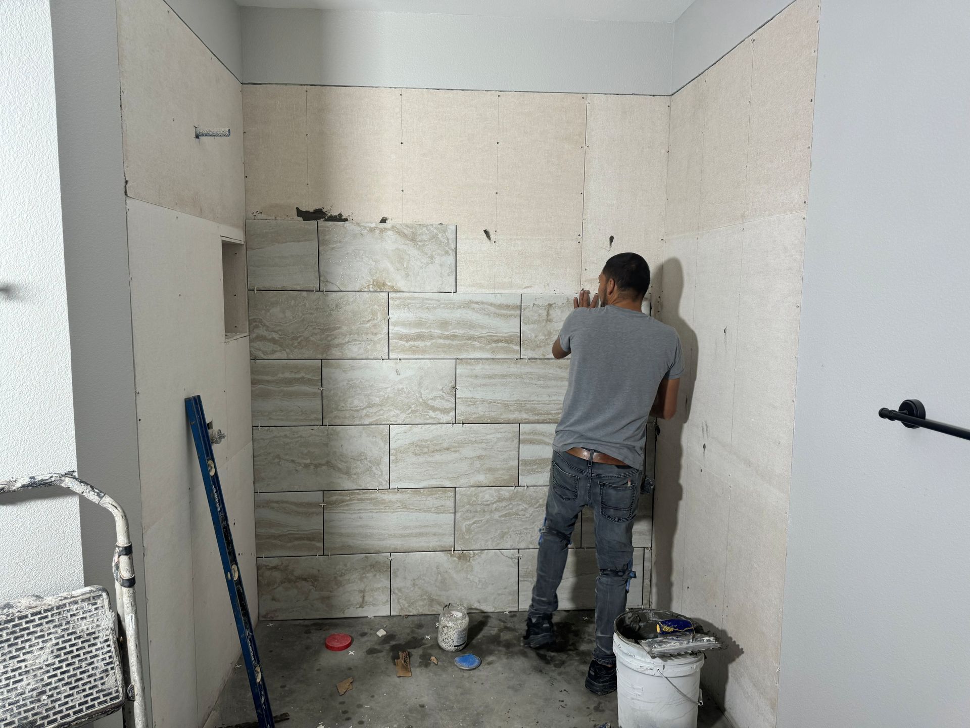 Worker installing large stone tiles on a bathroom wall