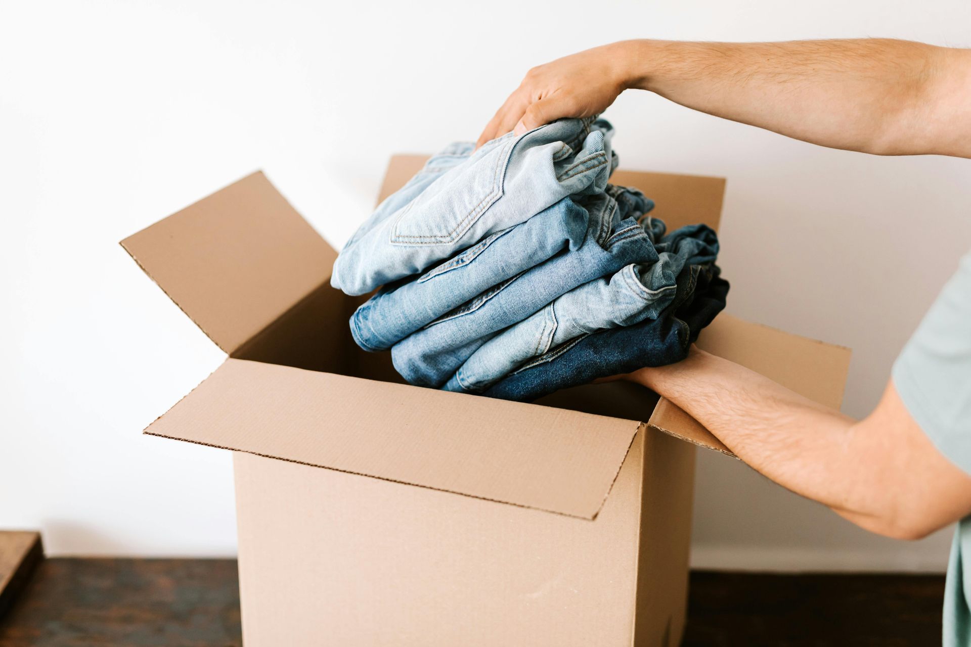 A person is putting clothes in a cardboard box.