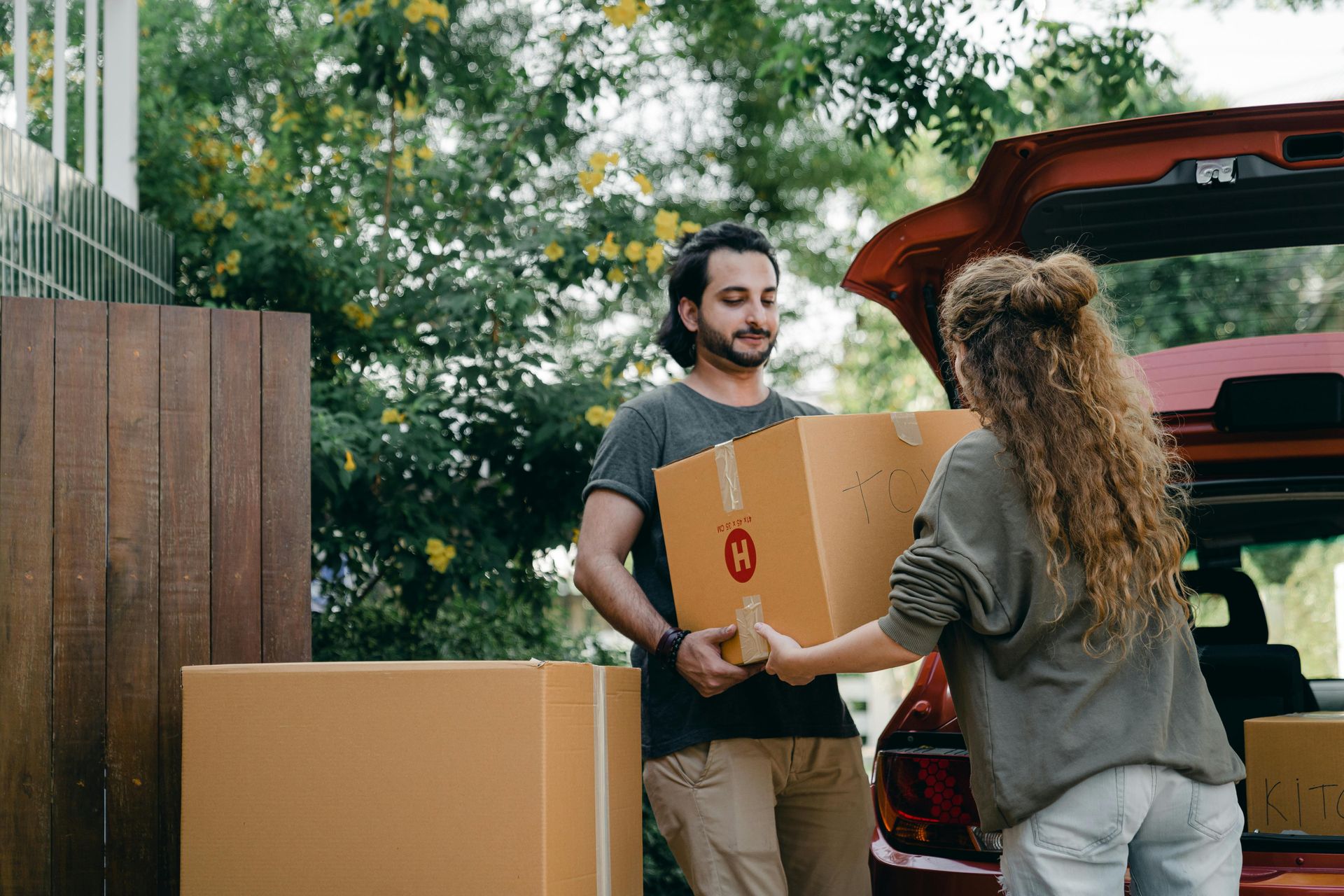 A man is giving a box to a woman in front of a car.