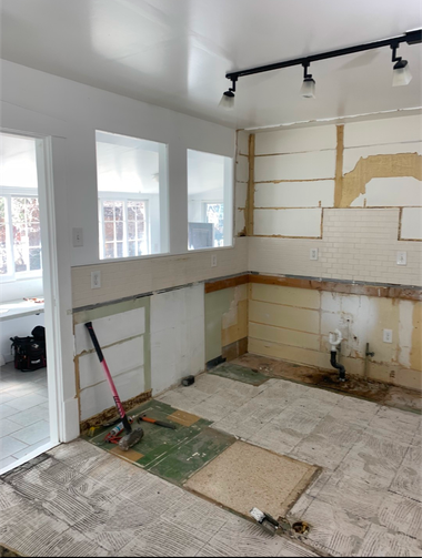 Kitchen under renovation with stripped walls, exposed cabinets, and construction debris on the floor
