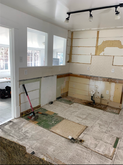 Partially demolished kitchen with exposed walls, floor debris, and a few tools near a doorway
