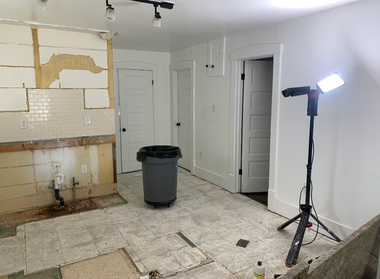 Renovated kitchen with exposed wall, trash can, and bright work light on a tripod
