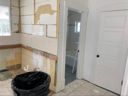 Partially demolished kitchen with exposed walls, debris, and a black trash bag during renovation