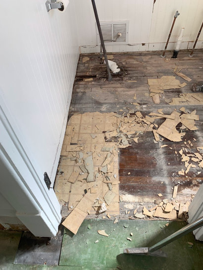 Damaged bathroom floor with peeling linoleum and exposed subfloor boards.