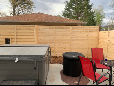 Backyard patio with hot tub, black fire pit, red chair, table, and wooden privacy fence