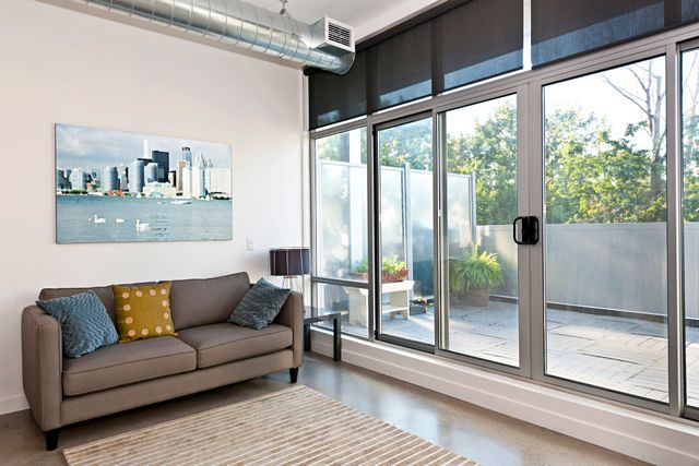 Un soggiorno moderno con divano grigio, cuscini decorativi colorati, una stampa astratta alla parete e grandi porte scorrevoli in vetro.