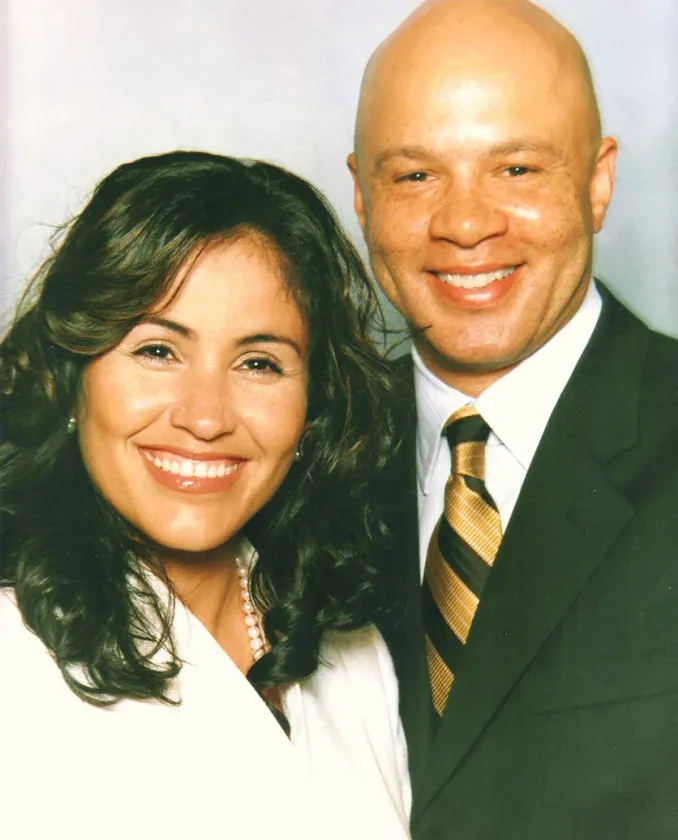 Two smiling people in formal attire posing against a plain background